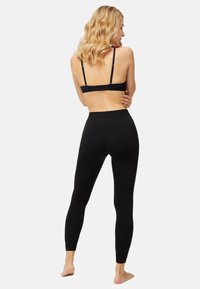 Leggings negros con una textura suave, diseño de cintura alta y ajuste elástico. Usados con un sujetador negro, mostrando tirantes ajustables y costuras mínimas.