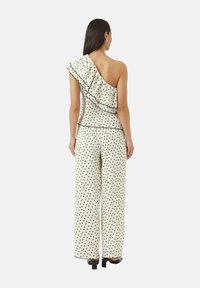 One-shoulder top with ruffle detail, cream fabric with black polka dots, paired with wide-leg pants, both with black trim and accents.