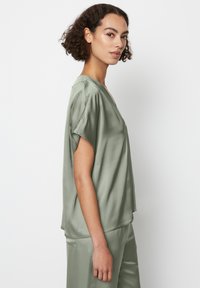 Blusa verde in satin con maniche corte e scollatura a V. Tessuto morbido con vestibilità comoda, accompagnata da pantaloni in satin coordinati.