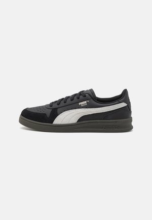 Chaussure de sport noire et grise avec une tige en suede texturé, des détails perforés et une semelle en caoutchouc épaisse arborant le logo PUMA.