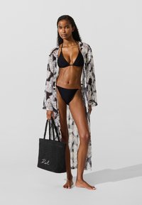 Melns bikini ar trīsstūrveida augšdaļu un zemas jostasvietas apakšdaļu, zem caurspīdīga kimono ar palmu rakstu. Melna pītā somiņa ar rokturiem.