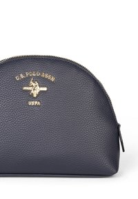 Pochette cosmetică cu fermoar de culoare bleumarin, realizată din piele texturată, având logo-ul și elementele de hardă aurii. Formă rotundă cu o bază căptușită pentru stabilitate.