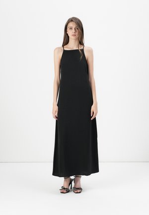Robe maxi noire à bretelles spaghetti, en tissu lisse, silhouette droite, longueur au sol, complétée par des talons à pois.