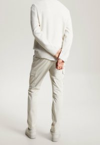 Vit stickad tröja, ljusa cargobyxor i off-white med två sidofickor. Avslappnad silhuett, slät textur och subtila sömnadsdetaljer.