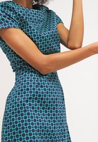 Robe à manches courtes en marine et bleu sarcelle avec un motif circulaire ; design épuré, taille ajustée et texture douce. Épaules accentuées.