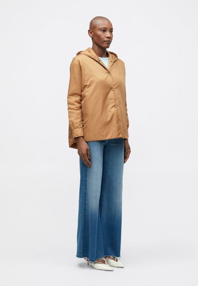 Tan hættejakke med knaplukning, parret med brede gradient blå denimbukser og hvide spidse hæle. Glat tekstur, afslappet design.