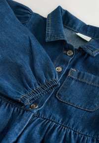 Denimkjole med korte puffærmer, frontknaplukning, brystlomme og samlet talje. Mørkeblå stof med synlige syninger.