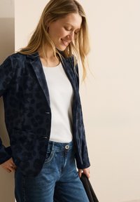 Marineblazer met een luipaardprint, twee voorkanten zakken en een notch lapel. Draag het over een witte blouse met een paar blauwe jeans. Gladde textuur.