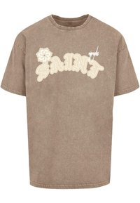 Brun oversized t-skjorte med rund hals, som har hvit og beige grafisk tekst "SAINT" og et blomsterdesign. Mykt, teksturert stoff.