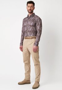 Brune paisley langemouwen shirt met button-down kraag, gecombineerd met beige cargobroek en lichtbruine laarzen.