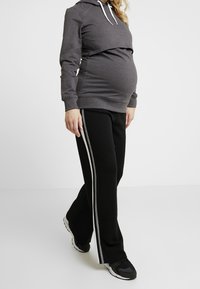 Szara krótka bluza z kapturem z białymi sznurkami i czarnym elastycznym pasem. Czarne spodnie dresowe z szarymi paskami po bokach i luźnym krojem.