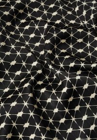 Tissu noir avec motif géométrique blanc de losanges et d’étoiles reliés, montré avec des plis et des froissements doux.