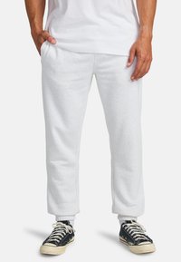Lichtgrijze joggingsbroek met elastische boorden, zijzakken en een losse pasvorm. Gecombineerd met zwarte sneakers met witte veters en een crèmewitte zool.