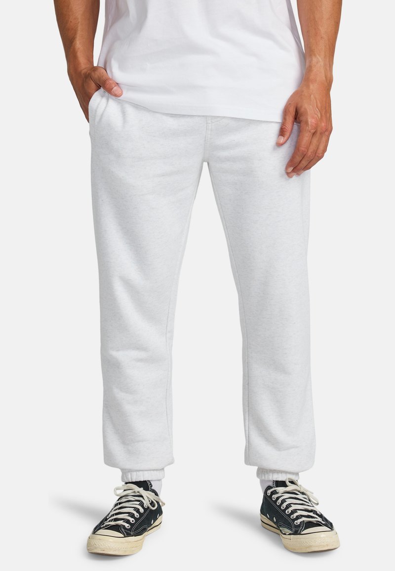 Lichtgrijze joggingsbroek met elastische boorden, zijzakken en een losse pasvorm. Gecombineerd met zwarte sneakers met witte veters en een crèmewitte zool.