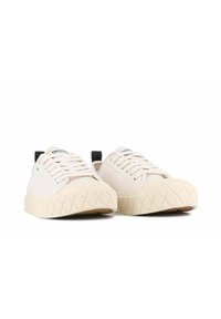 Světlé béžové tenisky s texturovanými, diamantovými podrážkami, bílými koženými svršky a černými akcenty na patě a logu. Šněrování.