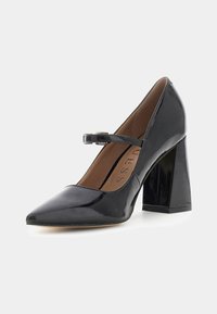 Décolleté in vernice nera con punta appuntita, tacco quadrato e cinturino Mary Jane regolabile. Interno con fodera beige.