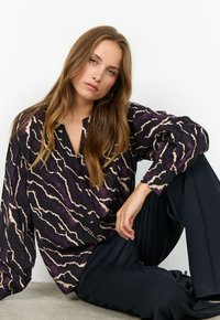 Långärmad blus i mörklila med ett vågigt mönster i gräddvitt och beige. Lättviktsmaterial med knappslå fram och avslappnad passform.