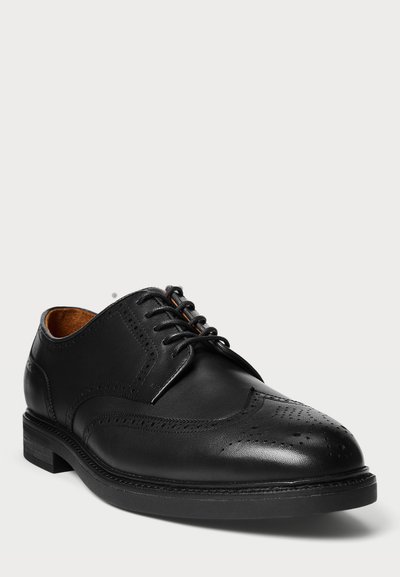 Pantofii bărbătești din piele neagră, tip wingtip brogue, cu perforații decorative și șireturi negre pe un fundal alb.