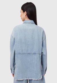 Šviesiai mėlynas džinsinis švarkas su laisvu kirpimu, turintis apsiūtas kraštines ir ilgomis rankovėmis, pasižymintis klasikinio stiliaus apykakle ir subtiliomis siuvimo detalėmis.