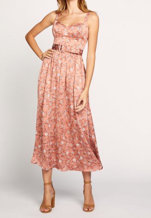 Femme portant une robe midi fleurie rose avec larges bretelles et une ceinture marron, associée à des sandales beige à talons hauts et à bride à la cheville.