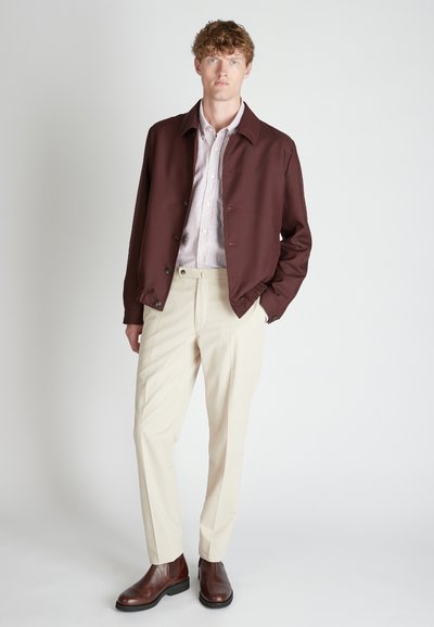 Chaqueta marrón con botones, camisa a rayas, pantalones crema y botas de cuero marrón. Tela suave con un ajuste entallado y un diseño estructurado.