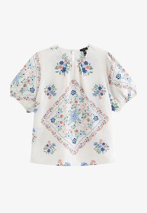 Blusa blanca de manga corta con mangas abullonadas y patrones florales multicolores dispuestos en forma de rombo en la parte delantera y las mangas.