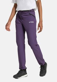 Pantaloni outdoor viola con un design aderente, tasca con zip e cintura elasticizzata; abbinati a scarpe da ginnastica nere.