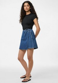 Tummansinisestä denimpinnoitteesta valmistettu kietaisuhame, jossa on sidottava vyötärö. Hameessa on leikkauksen muodikas flare ja raaka helma. Musta istuva lyhythihainen paita viimeistelee asun.