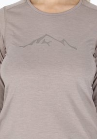 Camicia a maniche lunghe color marrone chiaro con una sottile grafica di montagne grigia sul petto. Il tessuto ha un aspetto liscio e testurizzato.