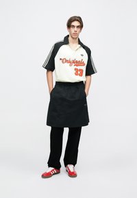 Svart og hvit kortermet polo med oransje bokstaver, svarte shorts og røde joggesko med hvite striper. Enkel, moderne atletisk stil.