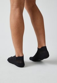 Calzini neri alla caviglia realizzati in un materiale liscio ed elastico con un motivo a rete per la ventilazione. Presentano un bordo arricciato per una vestibilità sicura.