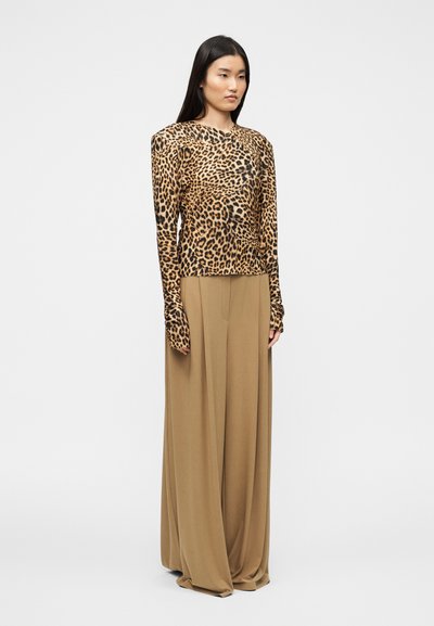 Μπλούζα με λεοπάρ μοτίβο και μακριά μανίκια, συνδυασμένη με αέρινες, καφετί παντελόνες φαρδιάς γραμμής. Λείο ύφασμα, δομημένοι ώμοι και επιμηκυμένα μανίκια.