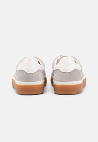 Grå semsket sneakers med hvite lærdetaljer, avrundet bak, og en sandfarget gummisåle. Slip-on design uten snøring.