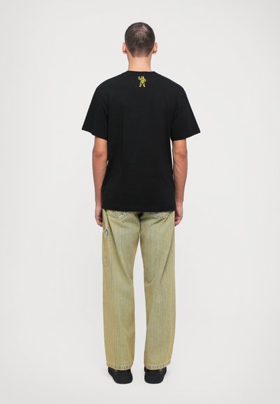Schwarzes T-Shirt mit einem kleinen gelben Grafikdesign auf dem Rücken, kombiniert mit lockeren, hellgrünen Jeans. Beide Kleidungsstücke haben einen lässigen Schnitt.