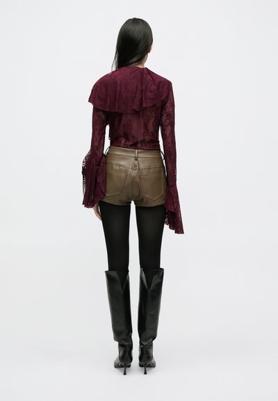 Bordowa koronkowa bluzka z falbankowanym kołnierzem, zestawiona z oliwkowozielonymi skórzanymi szortami i czarnymi kozaczkami do kolan na ciemnych rajstopach.