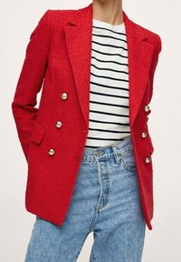 Blazer rouge texturé à boutons doubles en argent, associé à une chemise rayée et un jean taille haute bleu clair.