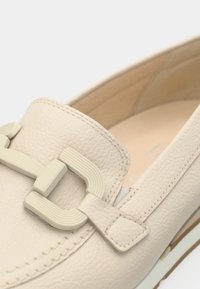 Μπεζ δερμάτινος μοκασίνι με υφή, λαστιχένια σόλα και εμφανές ορθογώνιο αγκράφα σε ανοιχτό χρώμα.