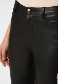 Black faux leather pants featuring a glossy finish, front zip and button closure, and side pockets. Smooth texture with minimal seams.