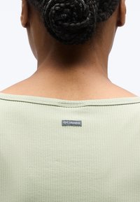 Πλάγια όψη ατόμου με πλεγμένο κότσο μαλλιών, φορώντας ανοιχτοπράσινο υφασμάτινο πουκάμισο με μικρή ετικέτα της μάρκας Columbia στο λαιμό.