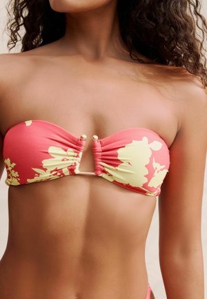 Korallkrāsa bikini tops ar dzeltenu ziedu rakstu, bez plecu siksniņām, ar priekšā rušinājumu un zelta akcentu detaļu centrā.