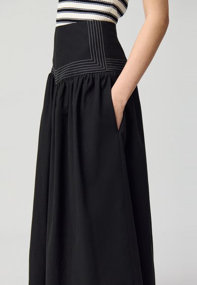 Jupe noire avec une partie supérieure fuselée présentant des coutures blanches contrastantes. Tissu fluide et froncé créant une texture douce avec des poches.