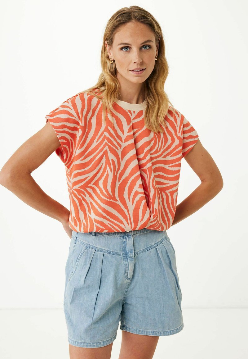 Top de manga corta con un estampado de cebra en naranja y beige, hecho de una tela suave. Combinado con shorts de mezclilla plisados en azul claro.