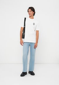 Hvit bomull t-skjorte med svart logo, lyseblå rette jeans og svarte sneakers. Minimalistisk design med avslappet passform og glatt tekstur.