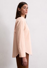 Camicia a maniche lunghe rosa chiaro con colletto a punta, caratterizzata da una vestibilità rilassata e fessure laterali all'orlo. Materiale in cotone morbido.