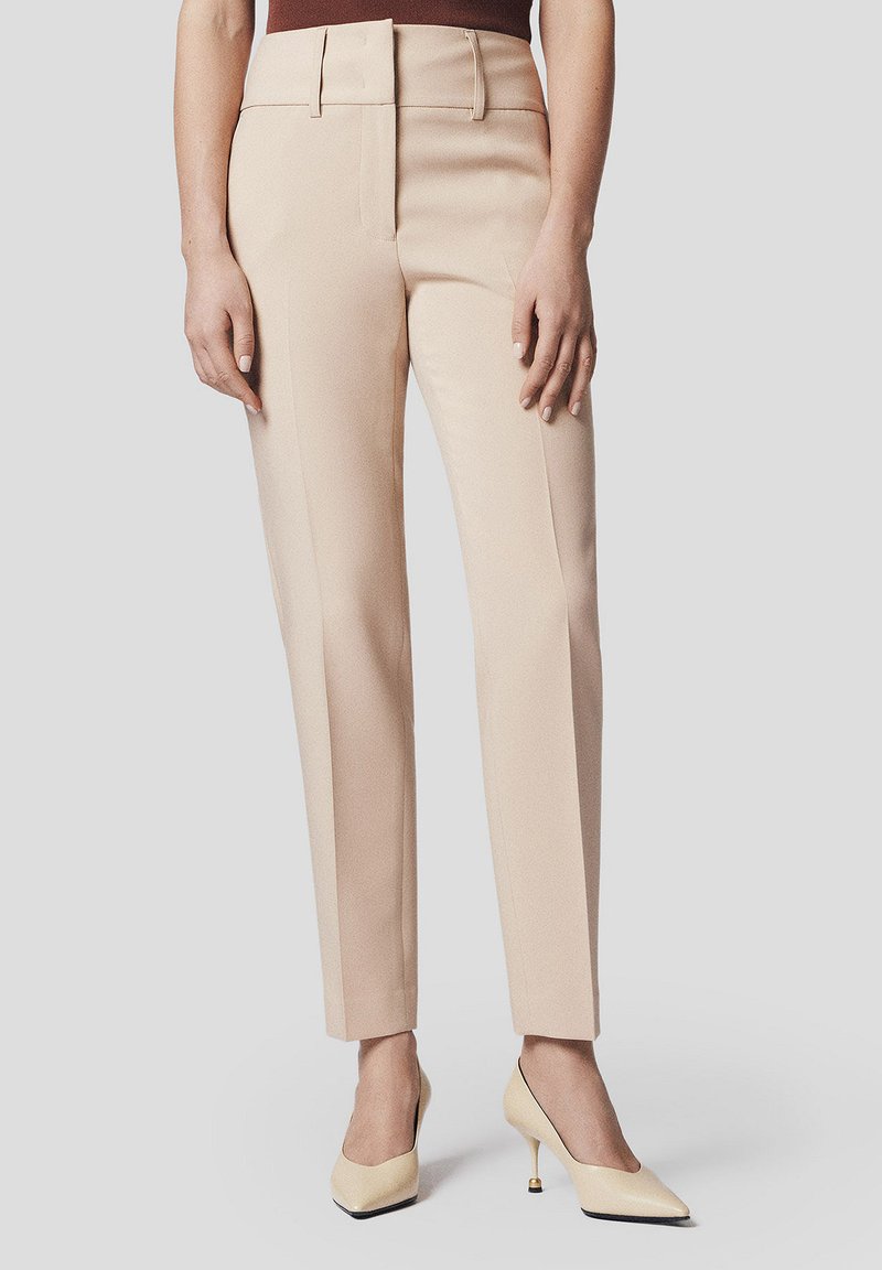 Beżowe dopasowane spodnie z wyższym stanem i prostymi nogawkami. Gładki materiał z bocznymi kieszeniami i paskiem. Połączenie z jasnymi szpilkami.