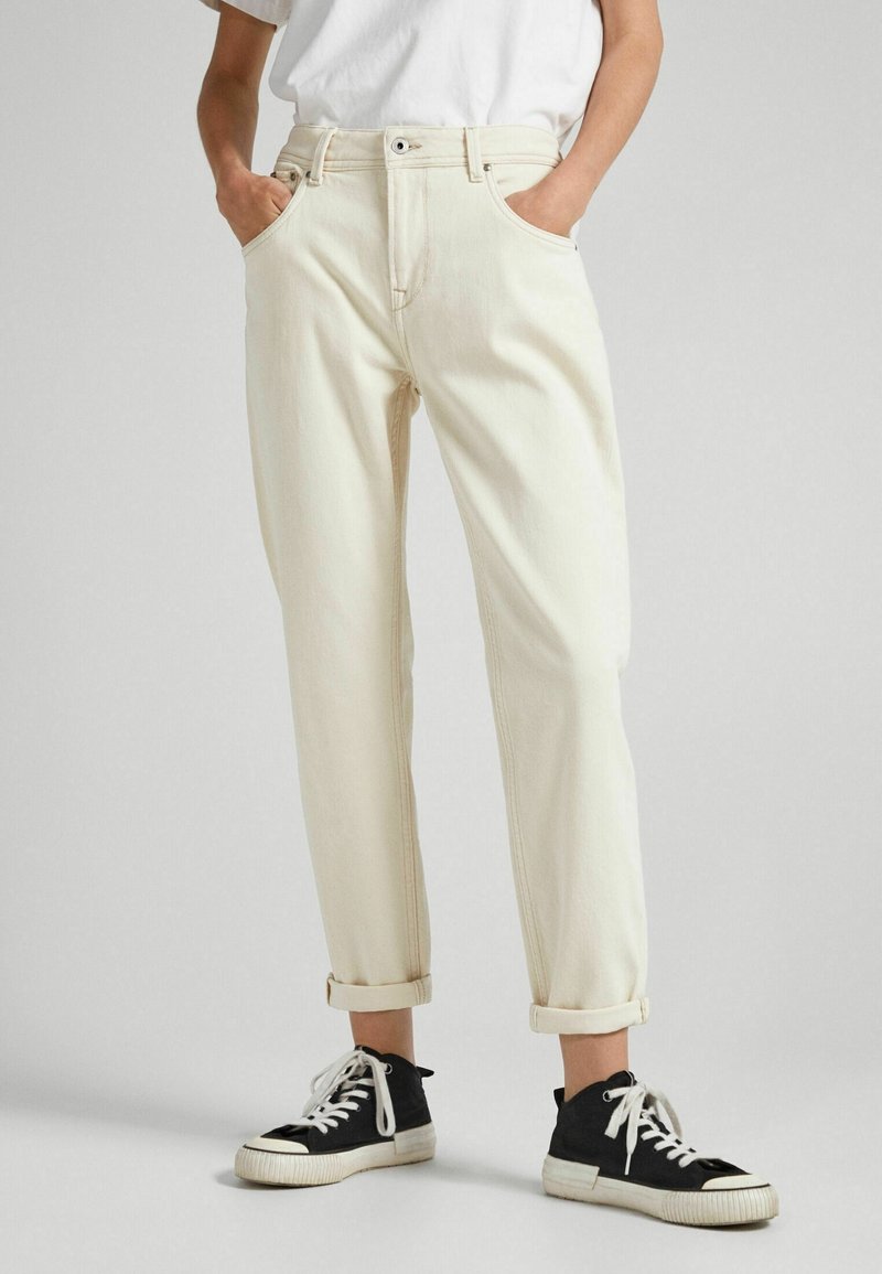 Kermanväriset, kapenevat farkut, joissa on kaksi etutaskua, käärityt lahkeet ja kontrastivärinen ompelu, yhdistettynä mustiin korkeisiin tennareihin.