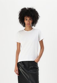 Hvid kortærmet t-shirt i blødt bomuldsstof med rund hals, parret med en sort lædernederdel. T-shirten har en afslappet pasform.