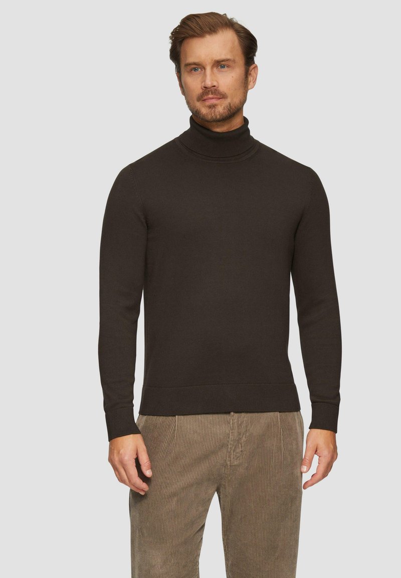 Pull en col roulé marron foncé avec une texture côtelée, doté de poignets et d'un ourlet ajustés. Porté avec un pantalon en velours côtelé marron clair.