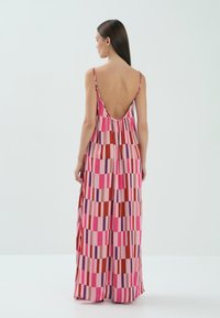 Maxi sukienka z cienkimi ramiączkami, z niskim tyłem. Wykonana z gładkiego materiału, prezentuje kolorowy, geometryczny wzór w odcieniach różu, czerwieni i fioletu.