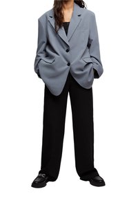 Blazer surdimensionné gris clair à deux boutons et poches avant, associé à un pantalon noir ample et des chaussures à plateforme noires.